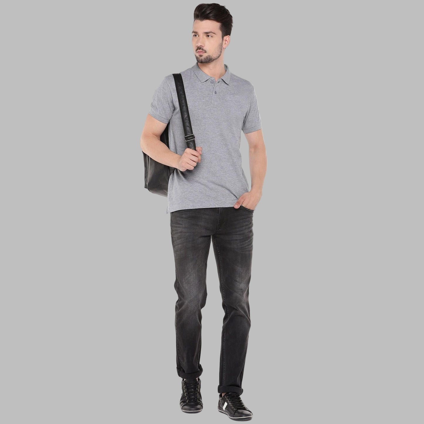 Man wearing a gray polo shirt, black jeans, and black shoes holding a black bag on a white background