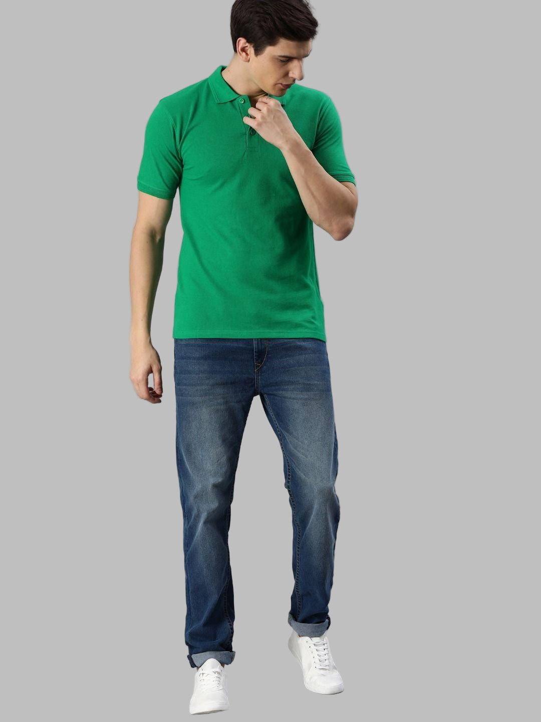 Man wearing a green polo shirt and blue jeans on a gray background