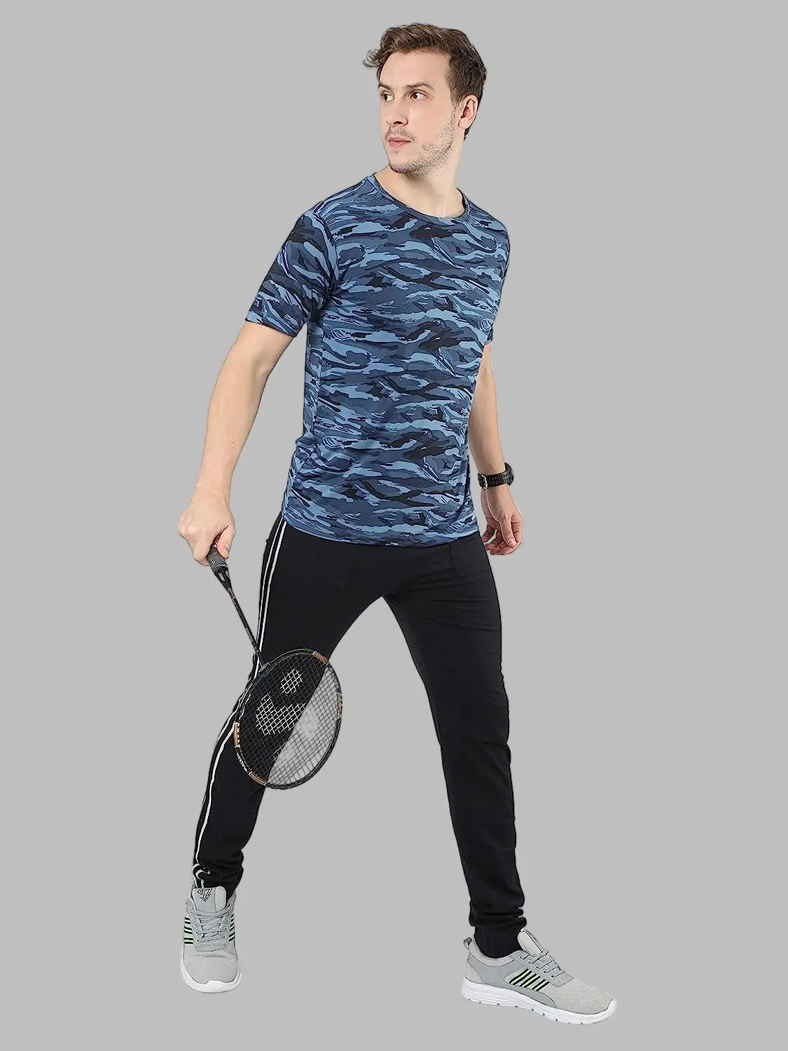 Man wearing a blue camouflage t-shirt and black pants, holding a badminton racket on a white background