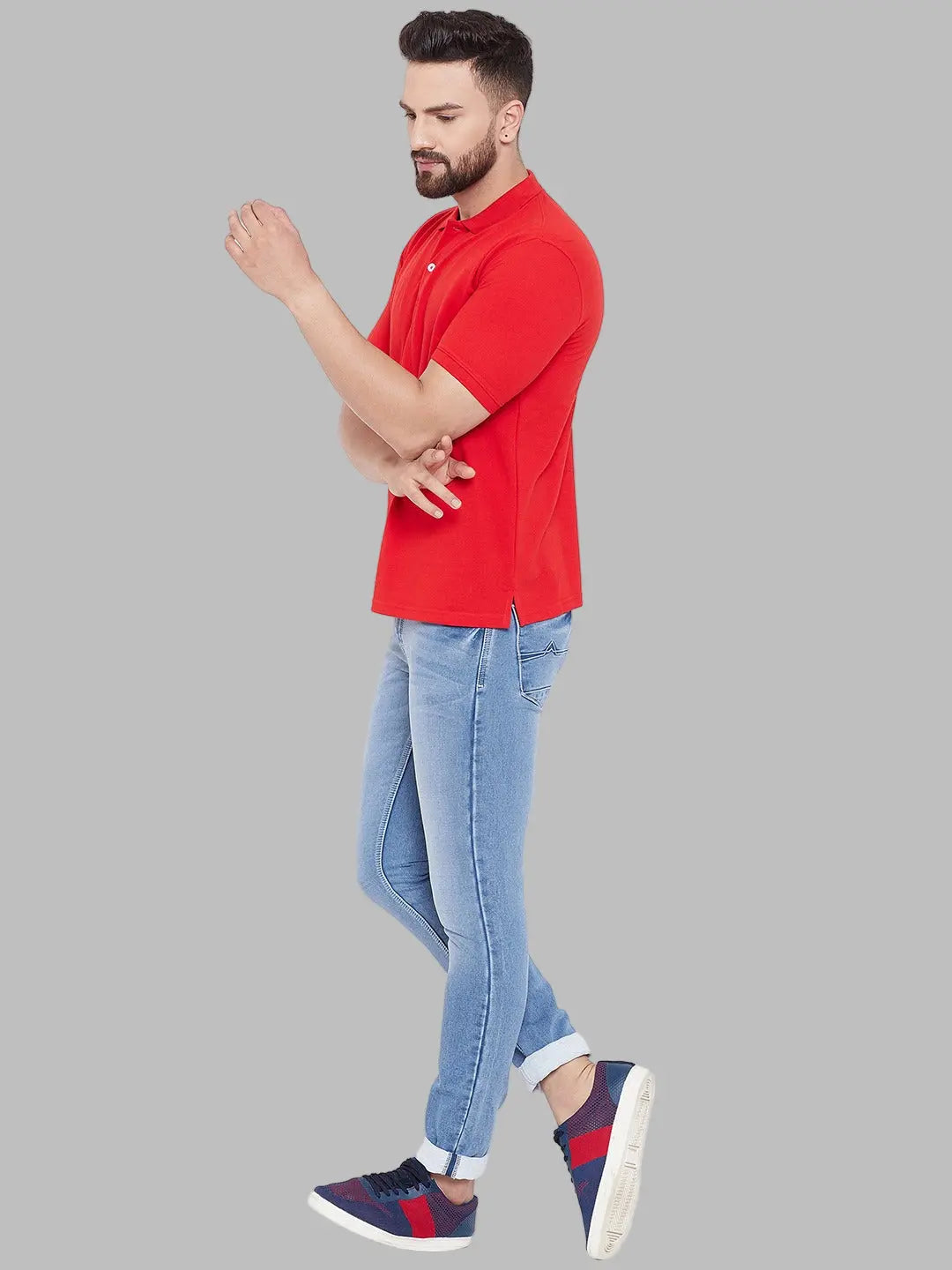 Man wearing a red polo shirt and light blue jeans against a white background