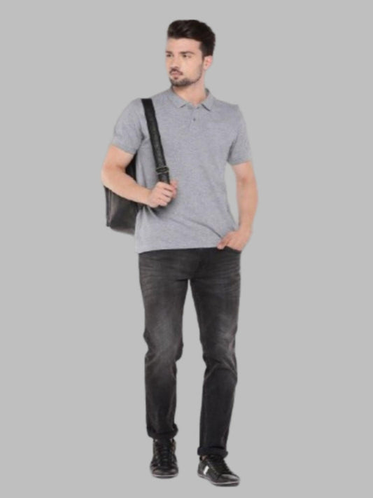 Man wearing a gray polo shirt and dark jeans holding a black bag on a gray background